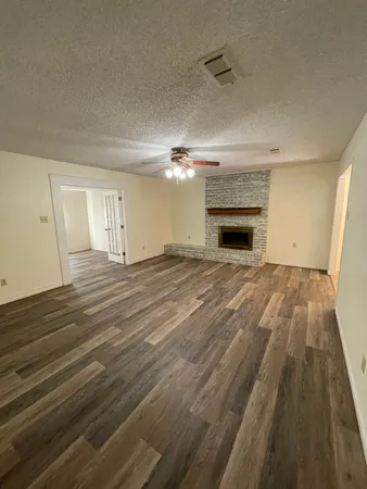 a view of an empty room with wooden floor fireplace and a window