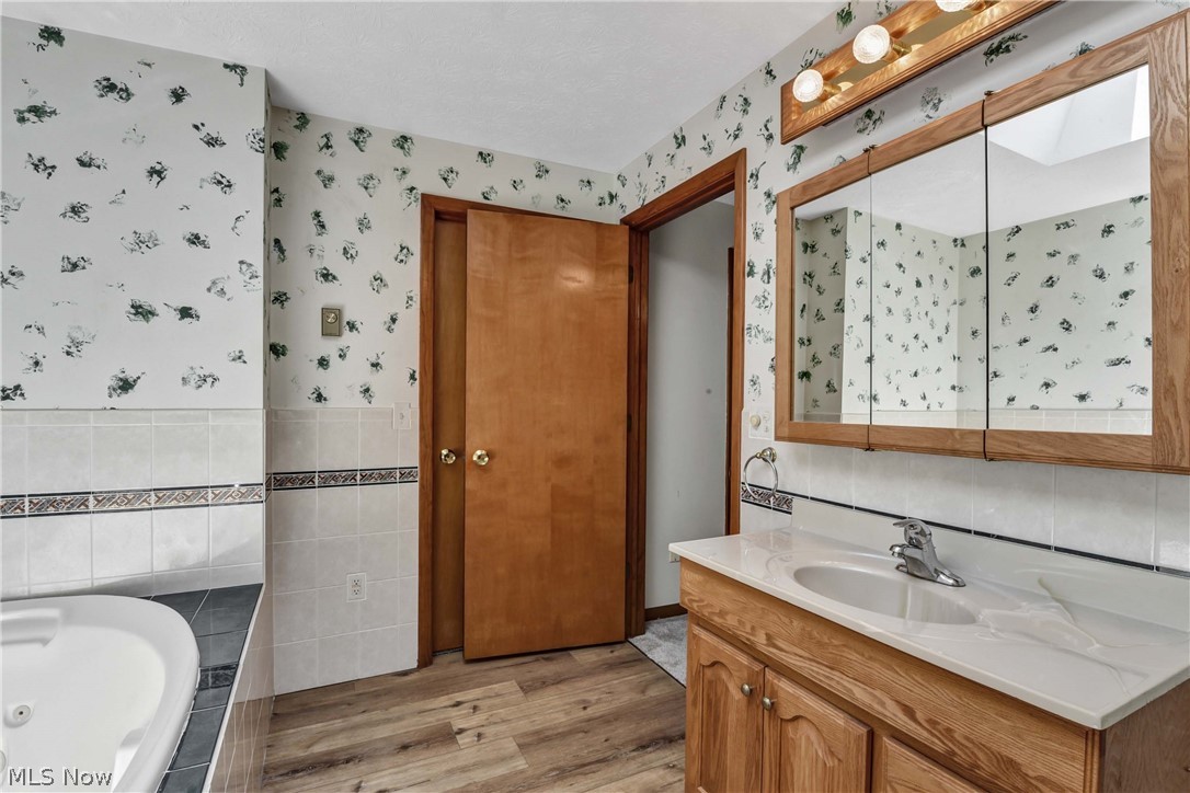 301 Crosse Road Amherst, OH 44001 - Photo 30 of 49 Bathroom featuring a soaking tub, wood-finish flooring, a vanity with a white countertop and integrated sink, a large mirrored medicine cabinet, and a multi-bulb vanity light fixture