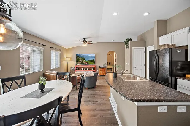 a living room with stainless steel appliances kitchen island granite countertop a table chairs and a refrigerator