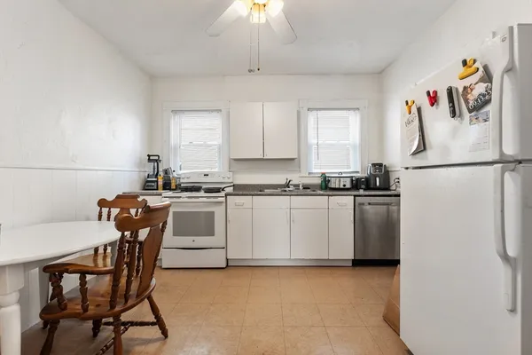a white kitchen with a refrigerator a stove a dining table and chairs