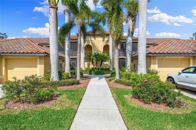 a view of a brick house with a yard plants and palm trees