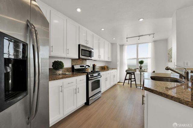 a kitchen with granite countertop a sink a counter top space stainless steel appliances and cabinets