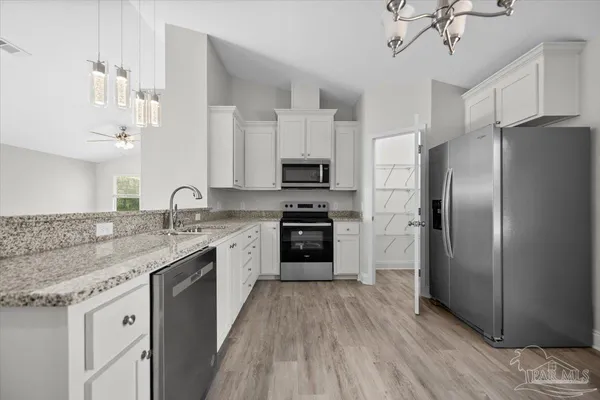 a kitchen with stainless steel appliances granite countertop a refrigerator a stove a sink and white cabinets with wooden floor