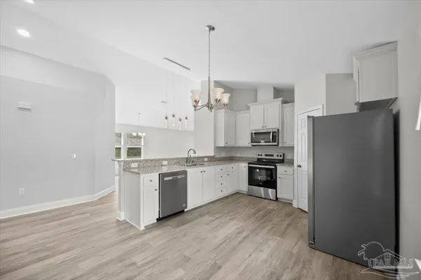 a kitchen with stainless steel appliances granite countertop a refrigerator a stove a sink and white cabinets with wooden floor