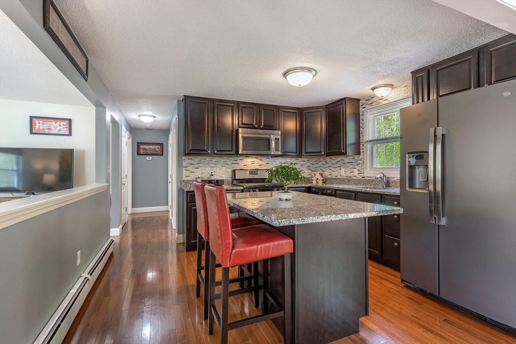 70 Parham Road Tyngsboro, MA 01879 - Photo 12 of 40 a kitchen with stainless steel appliances granite countertop a refrigerator a stove a sink a dining table and chairs with wooden floor