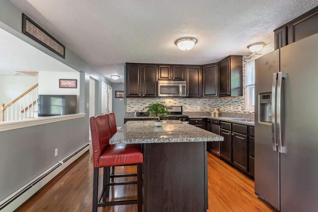 70 Parham Road Tyngsboro, MA 01879 - Photo 13 of 40 a kitchen with stainless steel appliances granite countertop a refrigerator a stove a sink a dining table and chairs with wooden floor