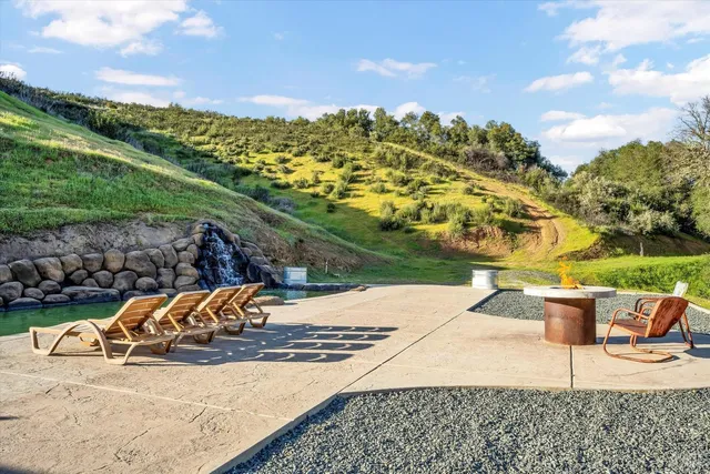 a view of swimming pool with seating space and trees in the background