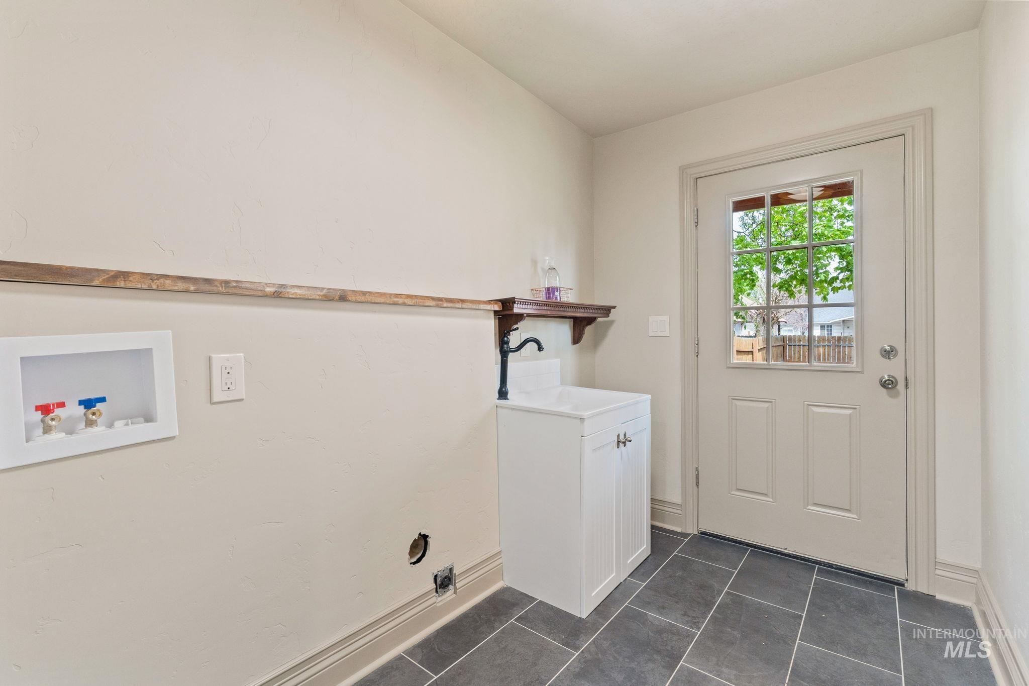 424 West Main Street Weiser, ID 83672 - Photo 11 of 30 Utility room with dark tile flooring, a white paneled door with windowpanes, and a utility sink with a black faucet