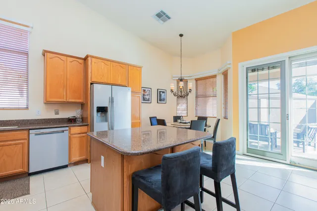 a kitchen with stainless steel appliances granite countertop a dining table chairs refrigerator and sink