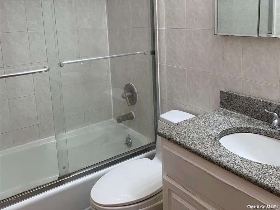 142-05 45th Avenue Queens, NY 11355 - Photo 2 of 9 Bathroom featuring bath / shower combo with glass door, toilet, vanity, and tile walls