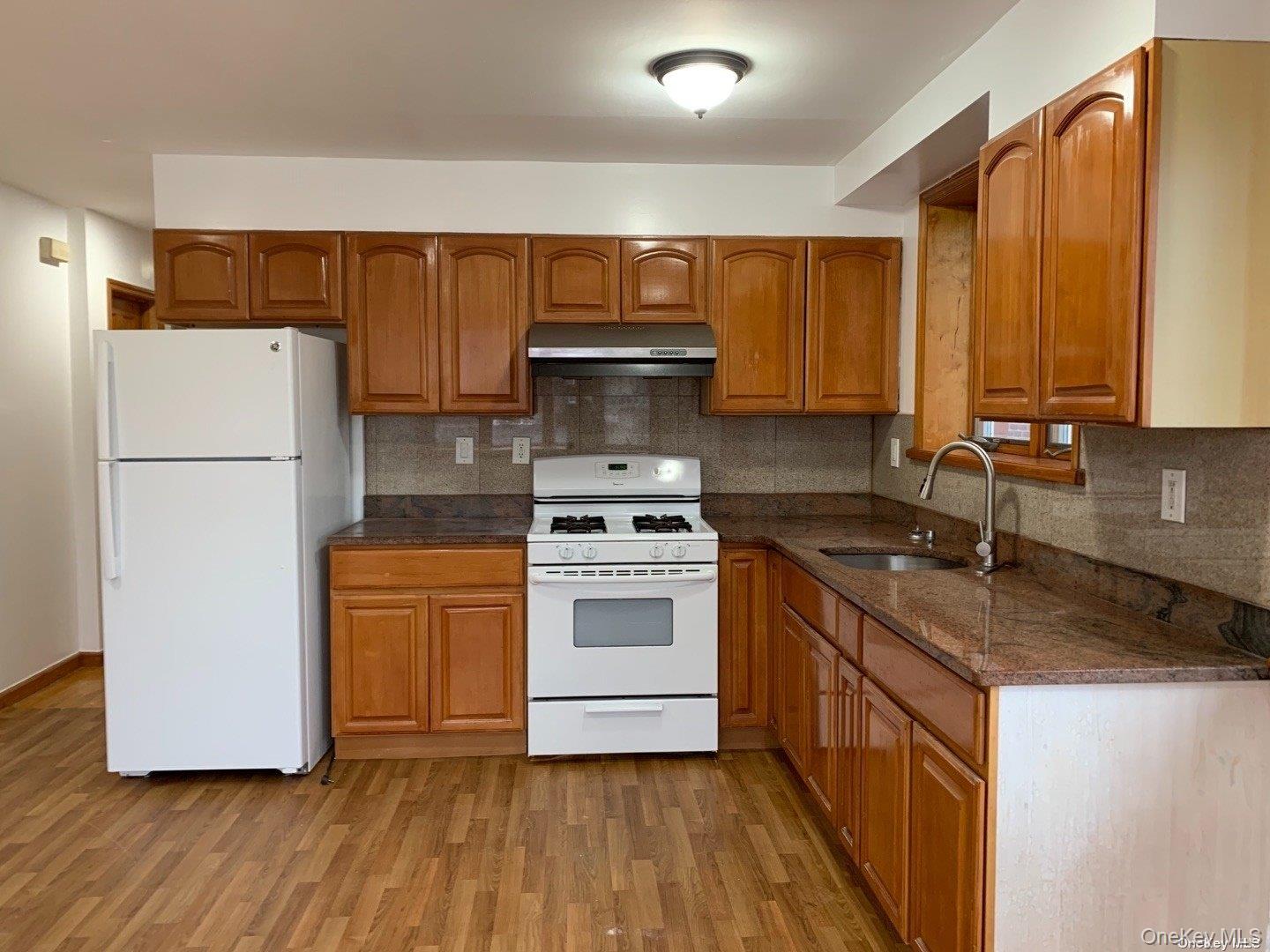 142-05 45th Avenue Queens, NY 11355 - Photo 5 of 9 Kitchen with white appliances, brown cabinets, under cabinet range hood, a sink, and light wood-type flooring