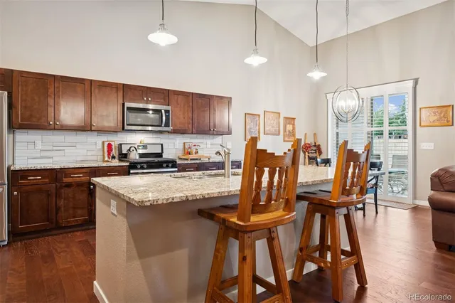 a kitchen with stainless steel appliances granite countertop wooden floors a stove top oven a sink with island and chairs