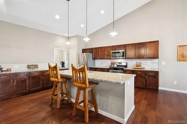 a kitchen with stainless steel appliances granite countertop wooden floors a stove a microwave a center island and furniture