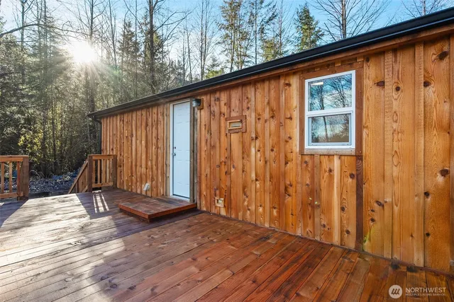 a view of a wooden house with large trees and lawn chairs under an umbrella