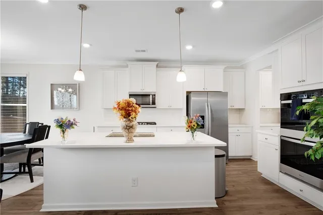 a kitchen with stainless steel appliances kitchen island granite countertop a refrigerator a sink a stove and white cabinets