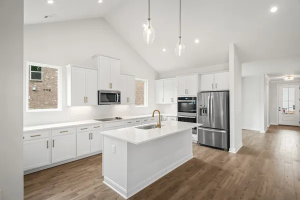 a kitchen with stainless steel appliances granite countertop a refrigerator a sink dishwasher a stove and white countertops with wooden floor