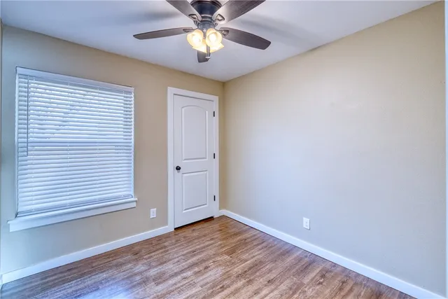 an empty room with wooden floor chandelier fan and windows