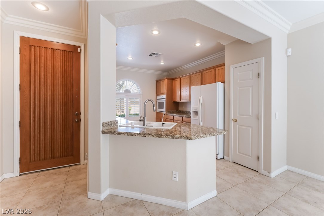 10481 Riverside Park Avenue Las Vegas, NV 89135 - Photo 11 of 51 Kitchen featuring white appliances, crown molding, light stone countertops, a peninsula, and wood finish cabinets