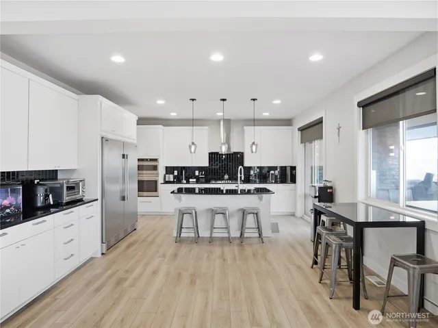 a kitchen with stainless steel appliances kitchen island granite countertop a stove a sink a refrigerator and white cabinets with wooden floor