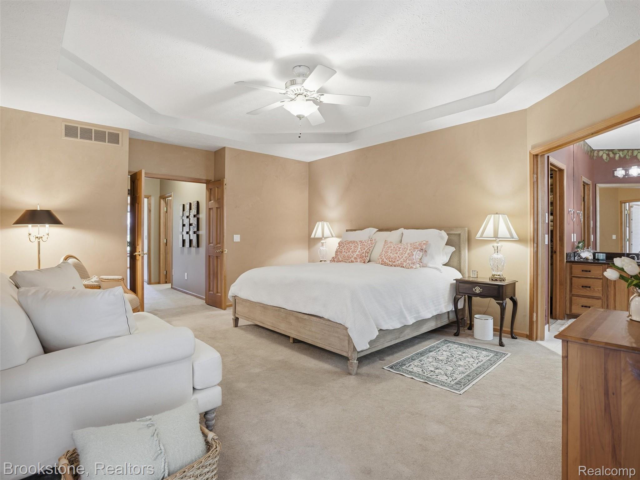 9523 Quail Ridge Run Brighton, MI 48114 - Photo 32 of 50 Carpeted room featuring a tray ceiling with a ceiling fan, light beige wall paint, and a doorway leading to an adjacent bathroom with a dark countertop vanity