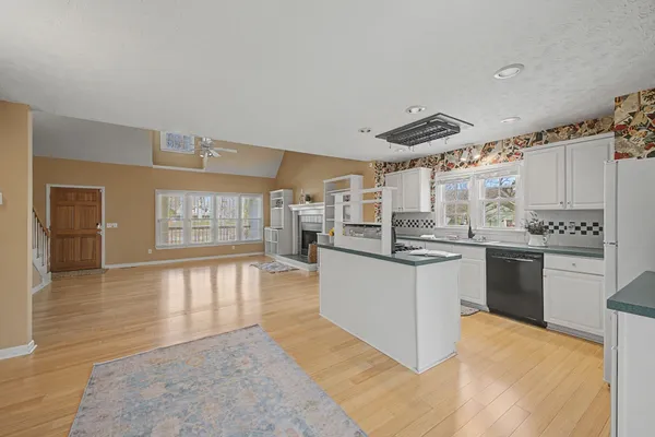 a large white kitchen with granite countertop a stove a sink dishwasher and a refrigerator with wooden floor