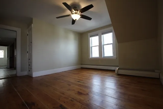 an empty room with wooden floor chandelier fan and windows