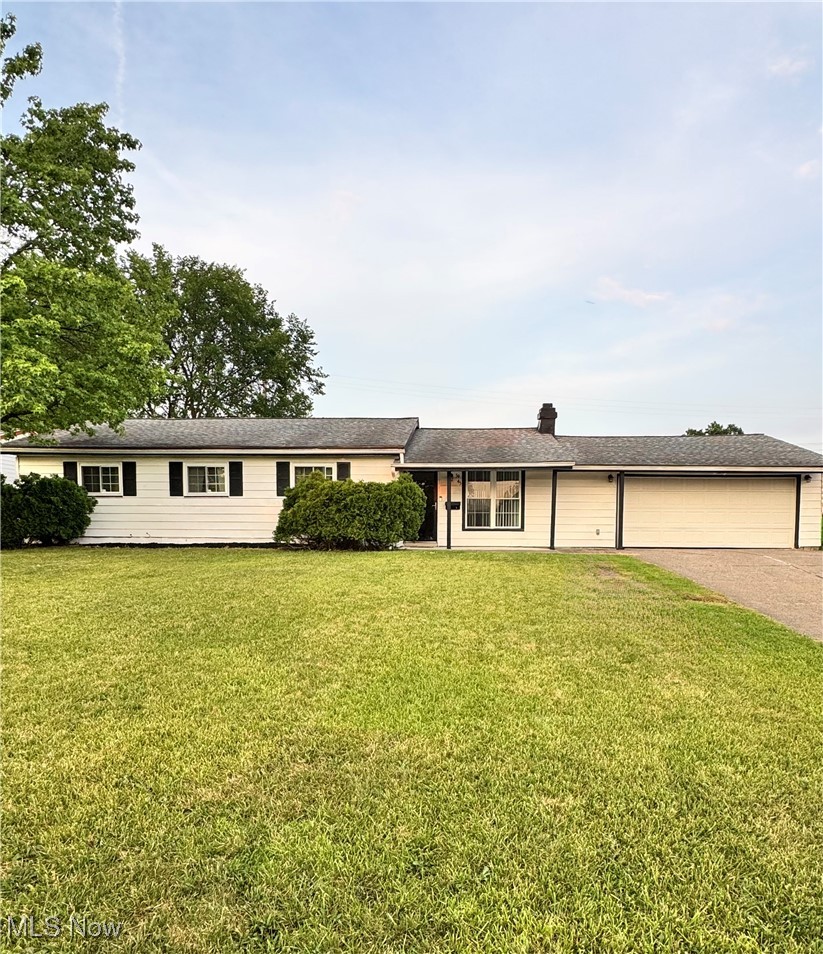 Ranch-style home with driveway, an attached garage, a front lawn, and a chimney