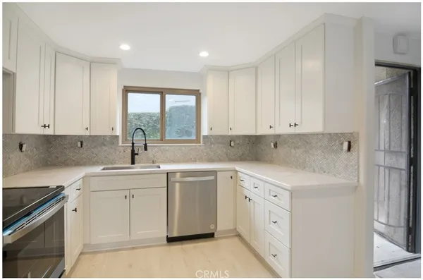 a kitchen with white cabinets appliances a sink and a window