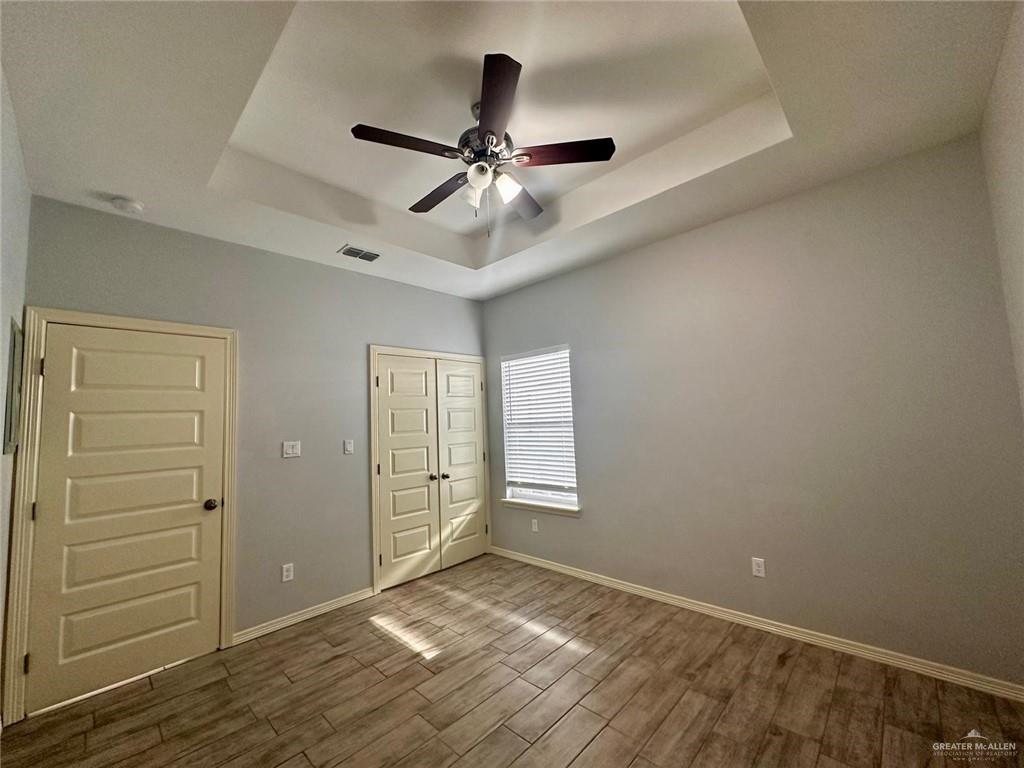 1503 West Heritage Drive, Unit 1 Pharr, TX 78577 - Photo 16 of 17 Unfurnished bedroom featuring a tray ceiling, dark wood-style floors, ceiling fan, and a closet