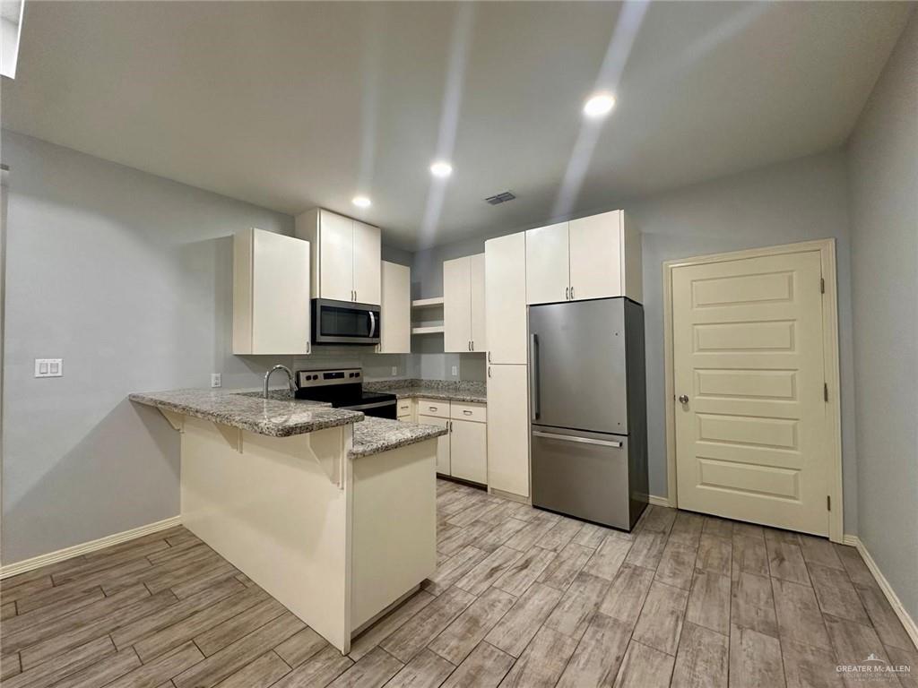 1503 West Heritage Drive, Unit 1 Pharr, TX 78577 - Photo 4 of 17 Kitchen with appliances with stainless steel finishes, a peninsula, light stone countertops, a breakfast bar area, and light wood-style floors