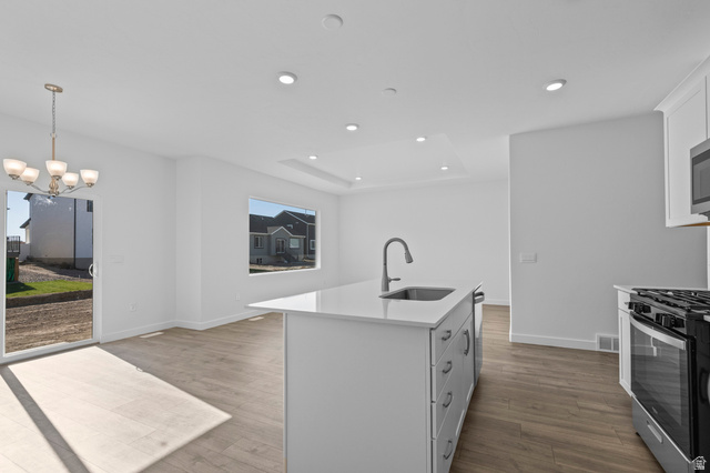 2823 North 710 West, Unit 16 Logan, UT 84321 - Photo 21 of 22 Kitchen with stainless steel range with gas stovetop, a kitchen island with sink, light stone counters, light wood-style flooring, and a tray ceiling