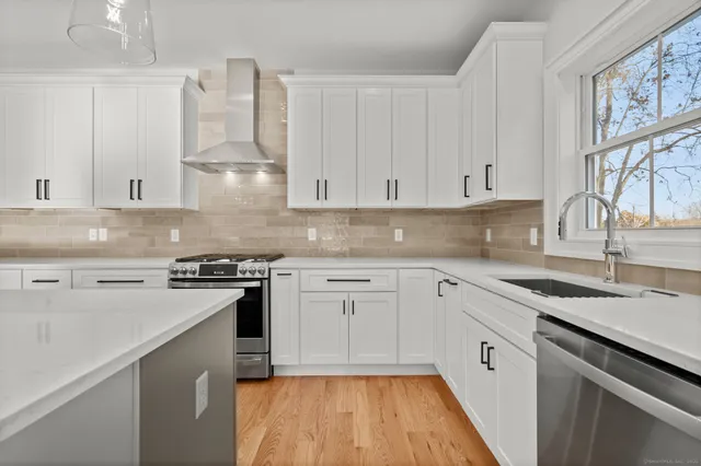 a large kitchen with stainless steel appliances granite countertop a refrigerator a sink dishwasher a stove and white countertops with wooden floor