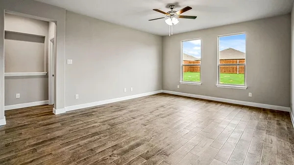 an empty room with wooden floor fan and windows