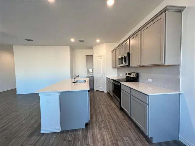 a kitchen with stainless steel appliances granite countertop a stove top oven a sink dishwasher and a refrigerator with wooden floor