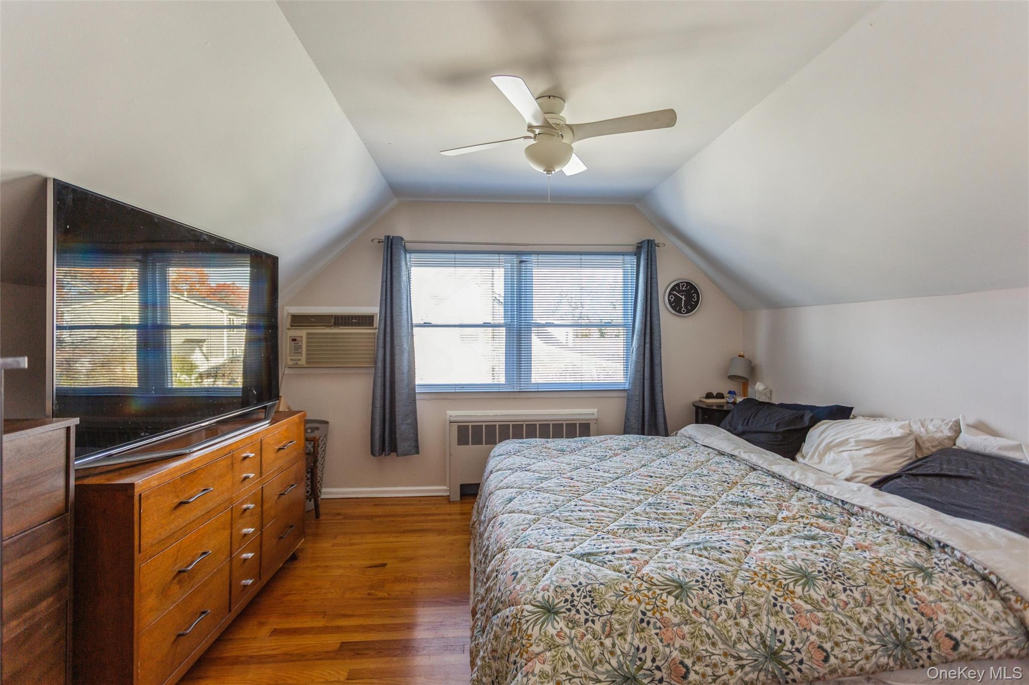 1531 Merrick Avenue Merrick, NY 11566 - Photo 17 of 26 Bedroom featuring wood finished floors, lofted ceiling, radiator heating unit, ceiling fan, and an AC wall unit
