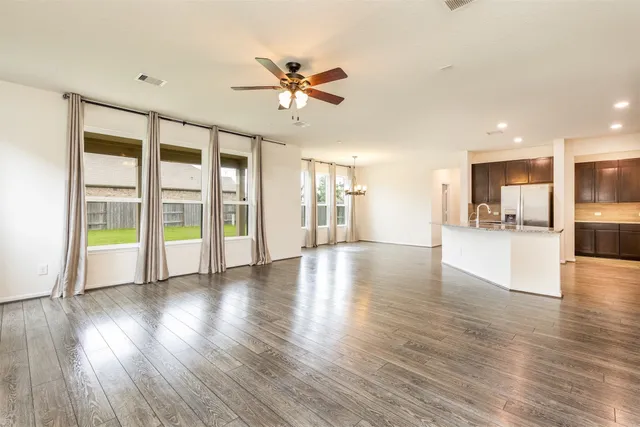 a view of an empty room with wooden floor and a kitchen