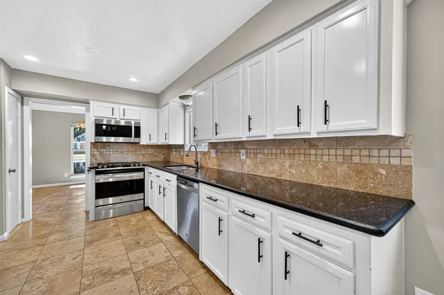 a kitchen with granite countertop white cabinets and stainless steel appliances