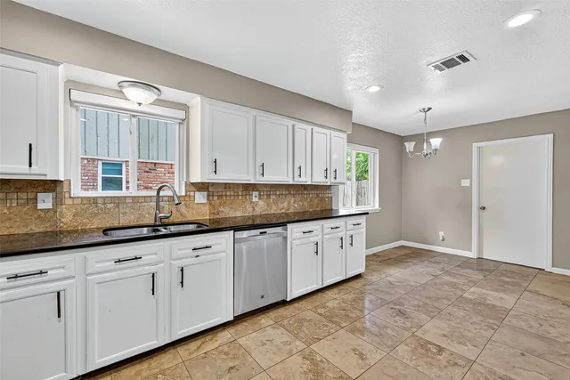 a large kitchen with granite countertop white cabinets and stainless steel appliances