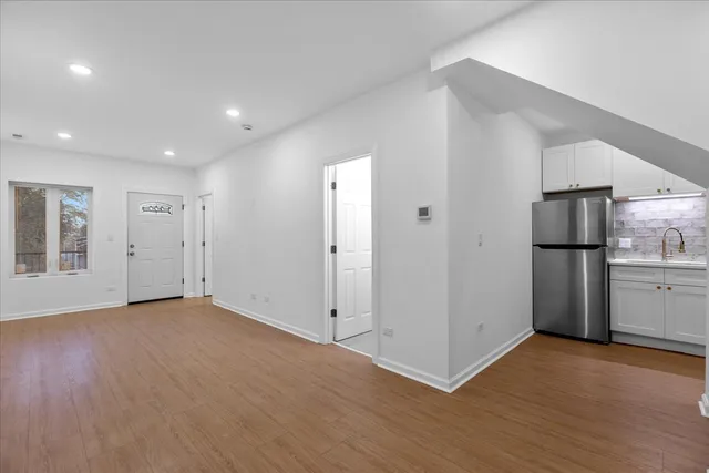 a view of an empty room with wooden floor and a kitchen
