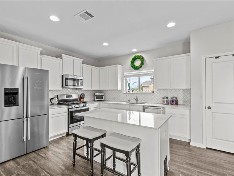 8201 Daisy Cutter Crossing Georgetown, TX 78626 - Photo 8 of 31 Kitchen with appliances with stainless steel finishes, white cabinetry, a kitchen bar, wood tiled floors, and a center island