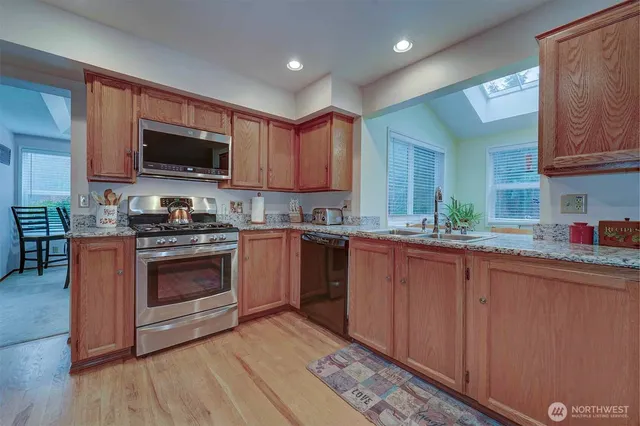 a kitchen with stainless steel appliances granite countertop a stove a sink dishwasher and a microwave oven with wooden floor