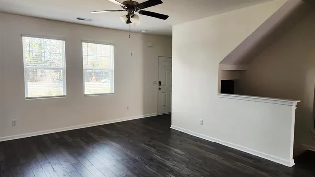 an empty room with wooden floor fan and windows