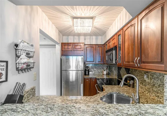 a kitchen with stainless steel appliances granite countertop a refrigerator a stove a sink dishwasher and wooden cabinets with wooden floor