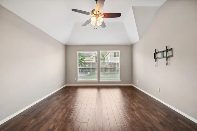 an empty room with wooden floor chandelier fan and windows