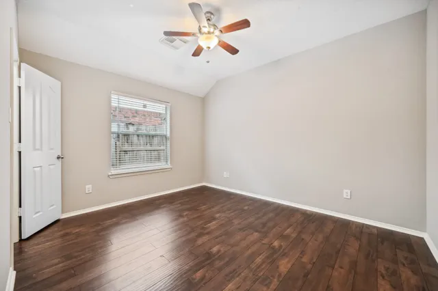 an empty room with wooden floor chandelier fan and windows