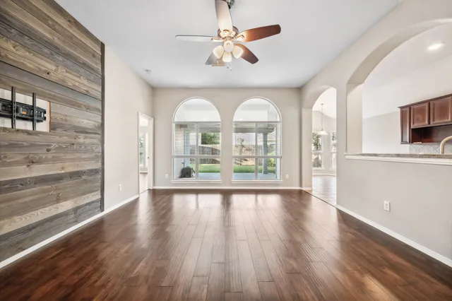 a view of an empty room with window wooden floor and a kitchen view