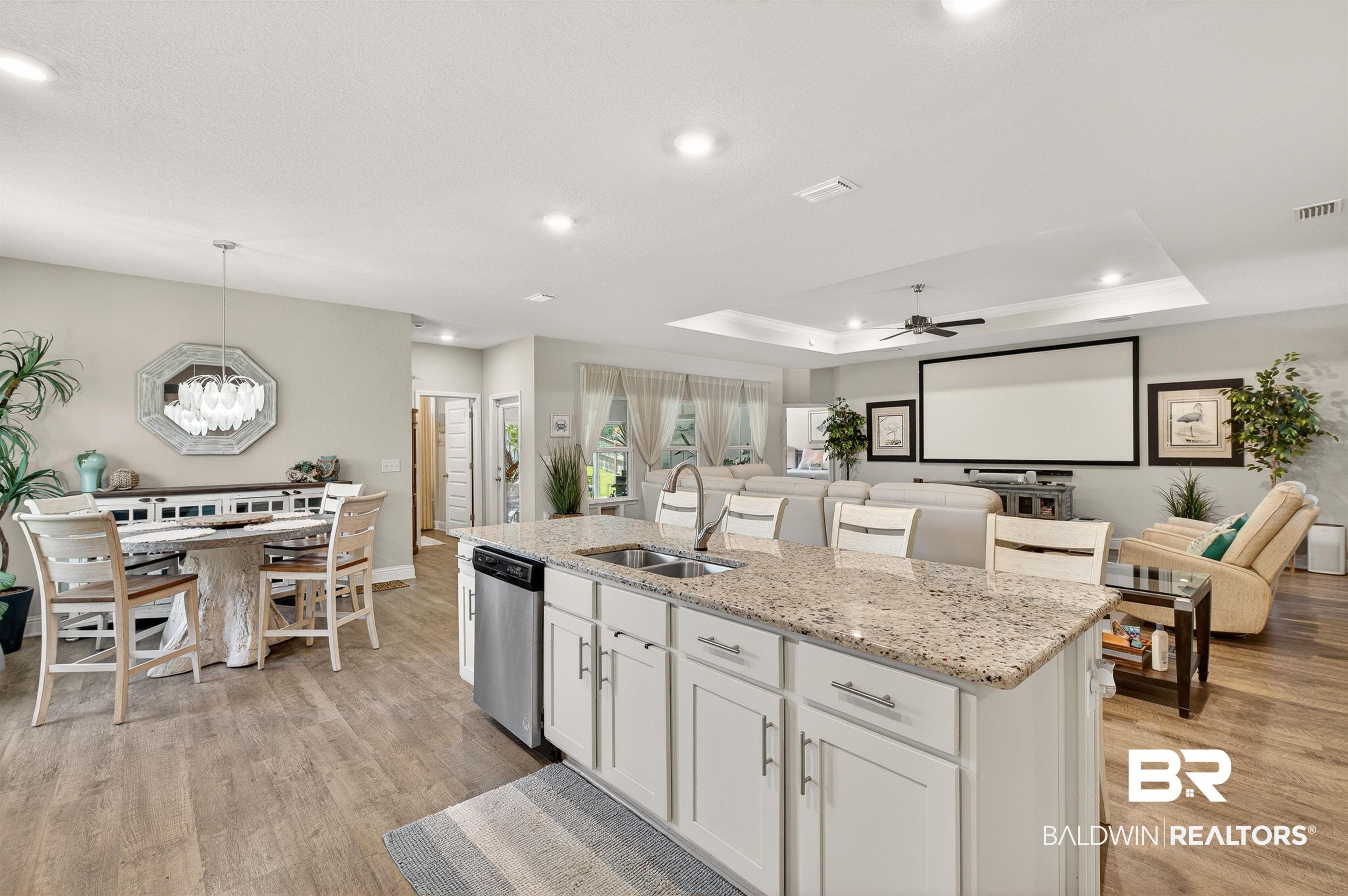 8735 Bronze Lane Foley, AL 36535 - Photo 12 of 58 Open-concept living space featuring wood-finish flooring, a kitchen island with granite countertop and integrated sink, stainless steel dishwasher, tray ceiling with recessed lighting, and a built-in projection screen