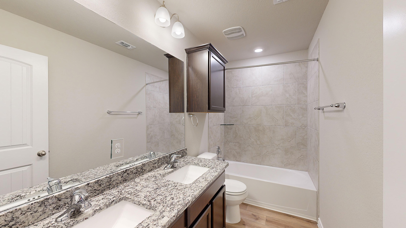 243 Water Wl Road Burnet, TX 78611 - Photo 20 of 23 Bathroom featuring a dual sink vanity with speckled countertops, a full-width mirror, and a bathtub with tiled surround