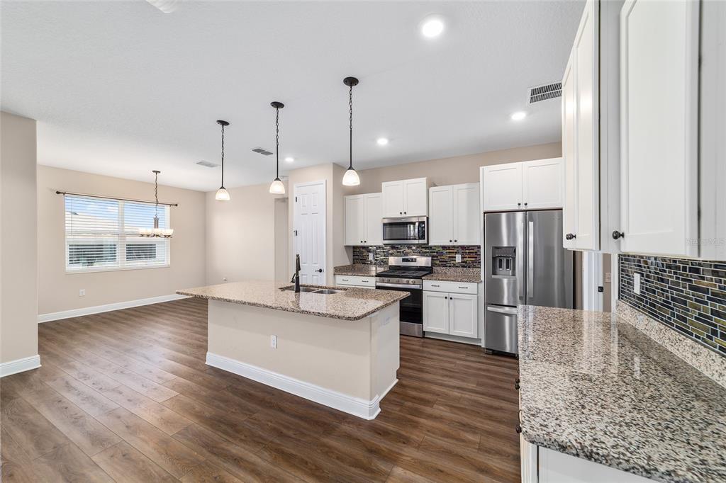 9778 Southwest 103rd Avenue Ocala, FL 34481 - Photo 26 of 57 a large kitchen with stainless steel appliances kitchen island granite countertop a stove a refrigerator a oven and a large island with wooden floor