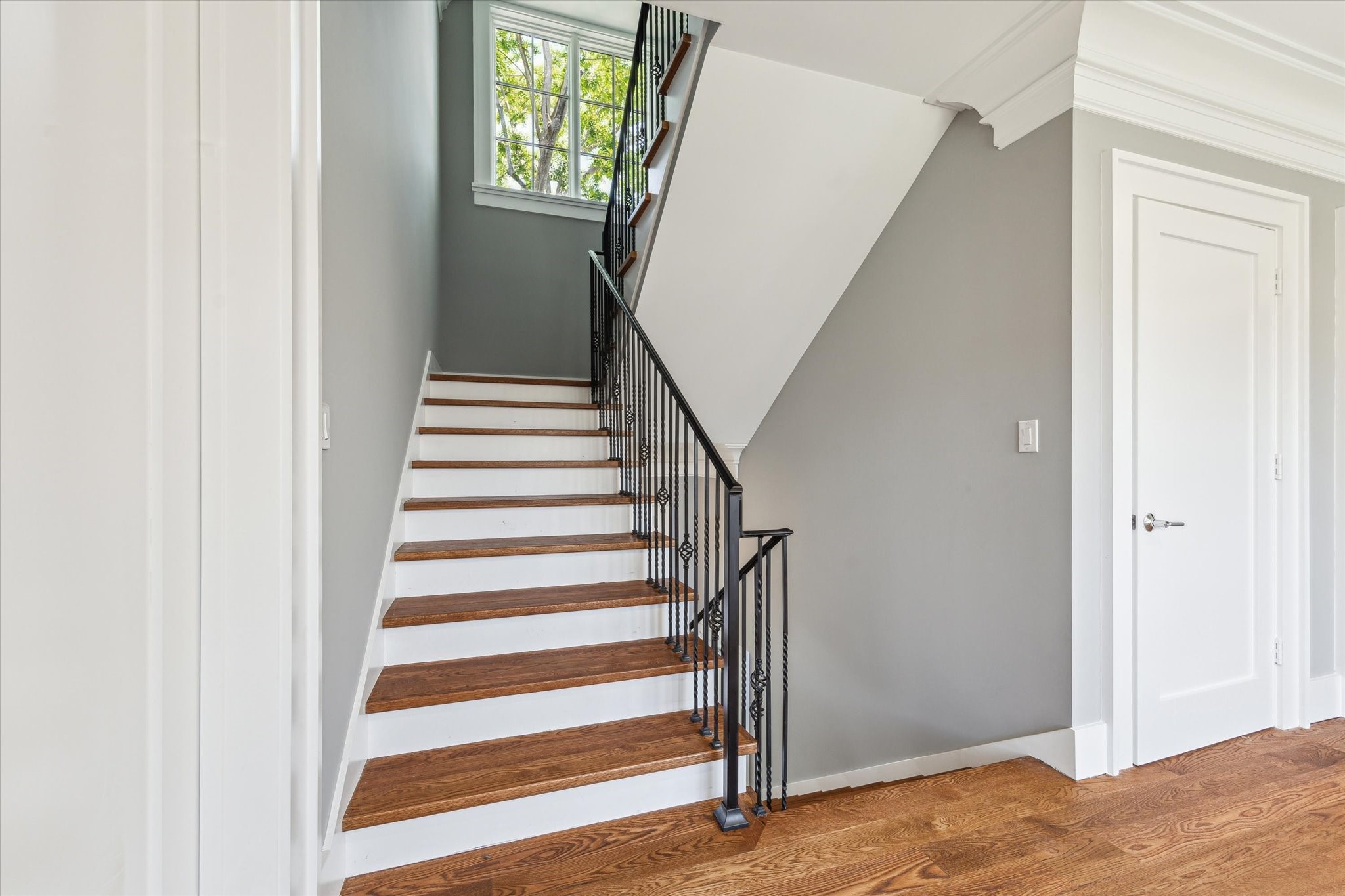 2216 Tangley Street Houston, TX 77005 - Photo 18 of 44 A bright and welcoming staircase with wooden steps and a black metal railing leads to the upper floor. The door to the right is the door for the elevator capable closet. The space features light gray walls, white trim, and a window providing natural light.